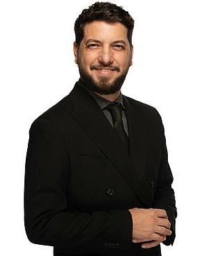 Tiago Arrais stands in front of a white background and smiles for a photo.