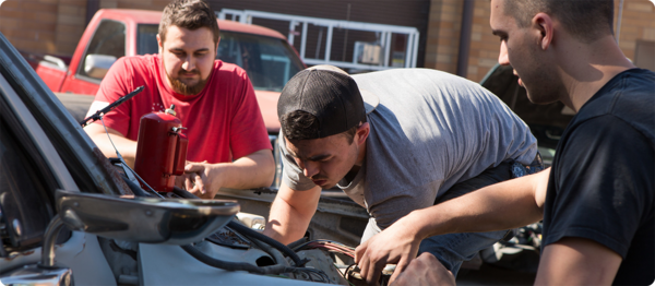 Three automotive students inspect the engine of a car to asses necessary 维修.